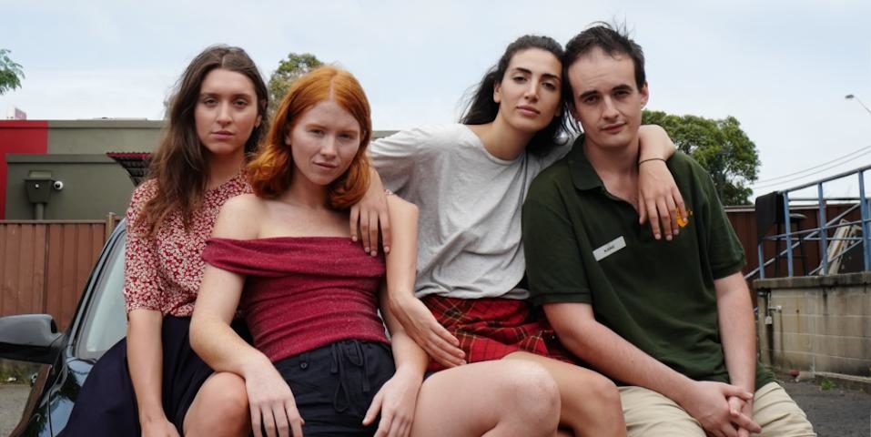 Four young actors, the main cast of the film, sit on the hood of a car, tight-knit.