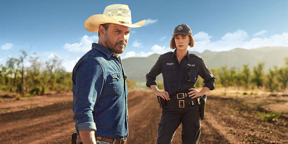 Promo shot from 'Mystery Road' a male Indigenous detective and female police officer standing on a cattle station